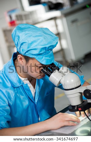 Factory worker in China looking through a microscope