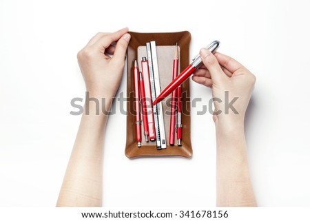 A woman hand hold a leather pencil tray(case, container) with variety red pencil, pen top view isolated white at the studio.