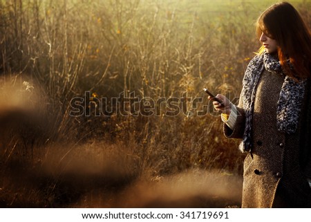 gorgeous stylish beautiful happy brunette girl looking at the telephone and smiling on a background of sunny autumn nature