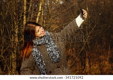 gorgeous stylish beautiful happy brunette girl taking selfie and smiling on a background of sunny autumn nature