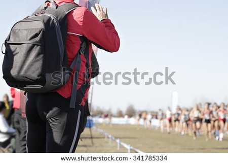 Woman taking a picture with her phone of some runners competing in a popular race