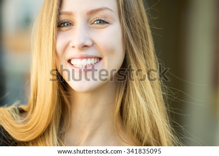 Closeup portrait of one beautiful happy smiling blonde young woman with long hair outdoor looking forward on blurred background, horizontal picture