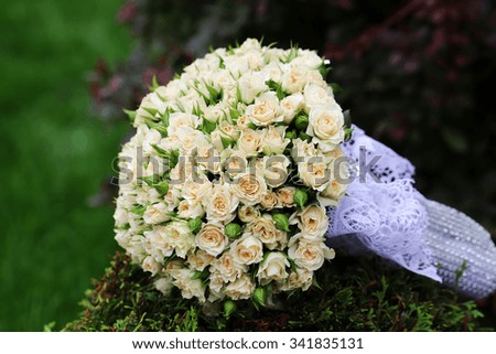 Closeup view of one beautiful fresh bright white yellow big wedding bouquet of rose flowers lying on green grass sunny day outdoor on natural background, horizontal picture