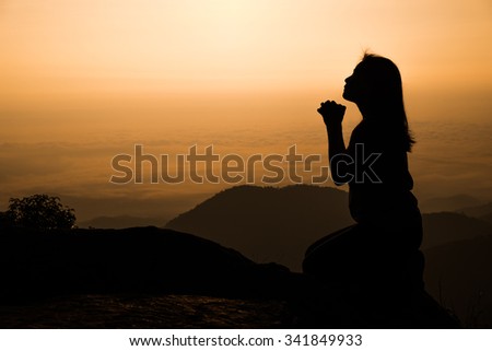 Silhouette of woman kneeling and praying over beautiful sunrise background