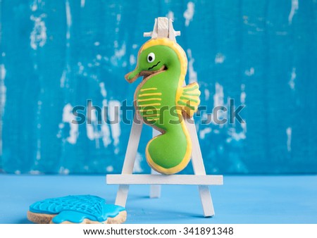 Homemade homemade gingerbread cookie in the shape of green sea Horse and shell on a blue wooden background. Space for text and selective focus.