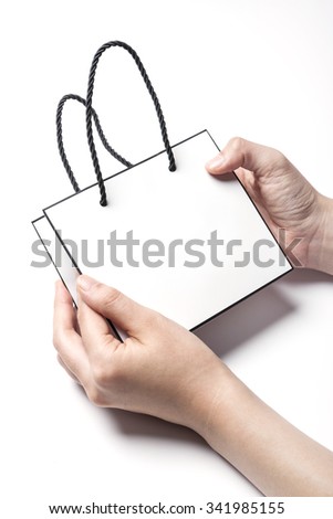 A woman hands hold a empty(blank, vacant, hollow) white small paper bag for cosmetics, accessory, top view isolated white at the studio.