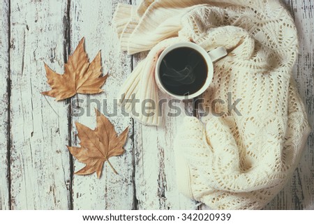 top view image of white cozy knitted sweater with to cup of coffee and autumn leaves on a wooden table. faded retro style image