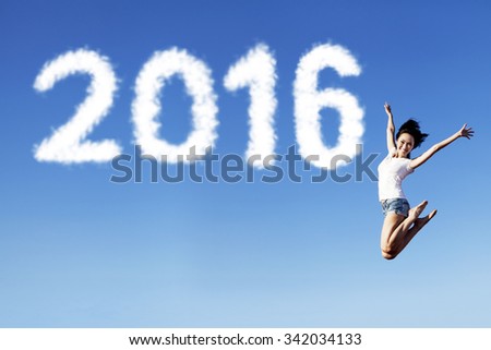Photo of a cheerful young woman jumping on the blue sky with clouds shaped numbers 2016