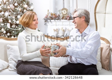 Man Giving Christmas Present To His Wife In White Interior. Christmas Theme