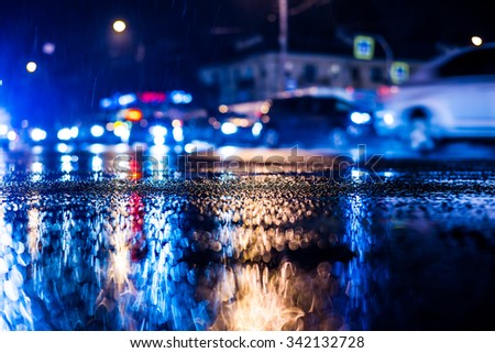Rainy night in the big city, dense traffic at a busy intersection, headlights of passing cars. View from the level of asphalt, in blue tones