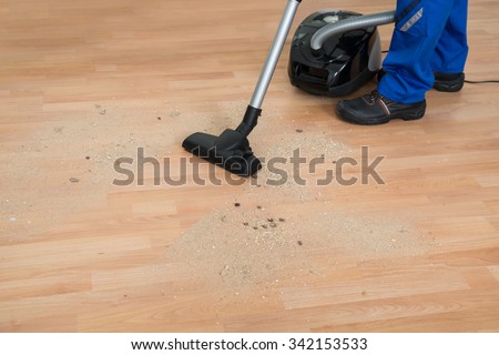 Low section of male janitor cleaning floor with vacuum cleaner in living room