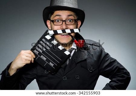 Detective in black coat with clapperboard against gray