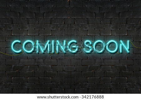"COMING SOON" neon sign shining on black brick wall,Business concept