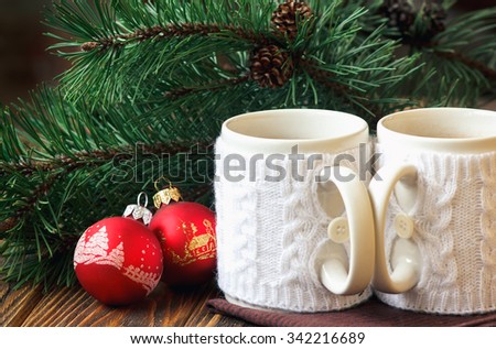 Christmas Decoration with fir twigs, red balls and cups of hot chocolate dressed in knitted warm winter mug holder on wooden background