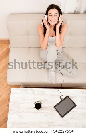 Young beautiful woman listening to music with headphones and a Tablet PC at home.