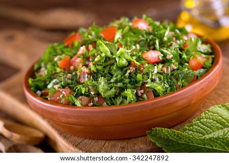 A bowl of delicious fresh tabouli with parsley, mint, tomato, onion, olive oil, lemon juice, and bulgar wheat. Royalty-Free Stock Photo #342247892