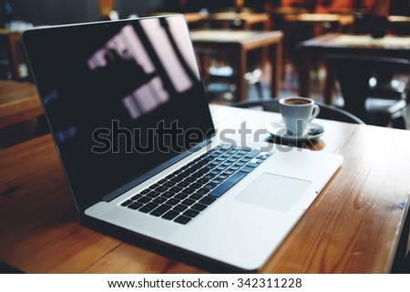 Portable net-book with copy space screen for your text message or promotional content, open laptop computer and cup of coffee lying on wooden table in modern cafe bar interior during morning breakfast