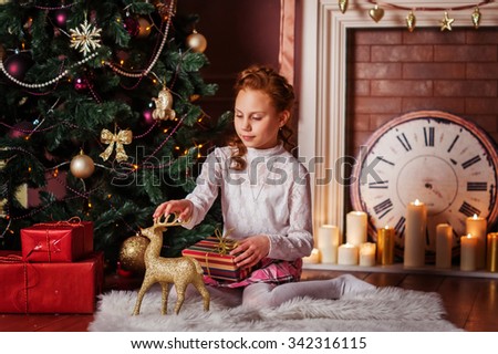 Christmas photo: cute baby girl with red hair near Christmas tree and fireplace with candles