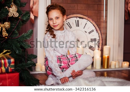 Christmas photo: cute baby girl with red hair near Christmas tree and fireplace with candles