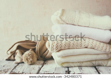 Stack of white cozy knitted sweaters on a wooden table. faded retro style image