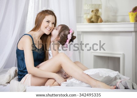 Cute little girl kissing her mother on a bed
