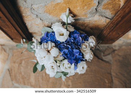 bouquet of blue flowers, white flowers and greenery stands at the stone wall