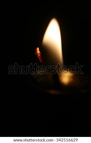 Photo closeup of single blurred soft warm flame of lighted fuse burning candlewick illuminating darkness on dark background, vertical picture