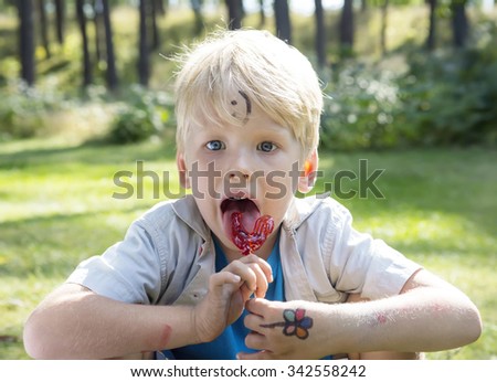 Concept of positive thoughts and emotions. Painted different funny pictures boy is sitting on green grass in nature and licking a lollipop. On the forehead shows (drawn) smile icon. 
