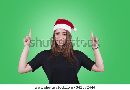 Young woman wearing Christmas hat pointing on green background
