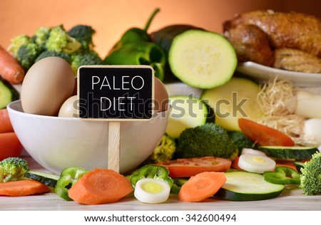 closeup of a signboard with the text paleo diet on a table full of different raw vegetables, a bowl with some chicken eggs and a chicken Royalty-Free Stock Photo #342600494