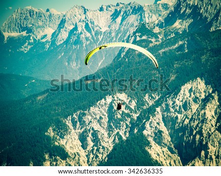 Paraglider flying over high and rugged range of Alps mountains. Cross process toned and Instagram stylized filtered stock photo with vignette.