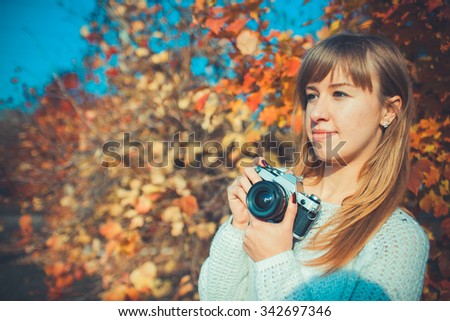 Young beautiful woman uses an old camera while walking through the park in autumn