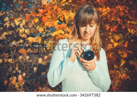 Young beautiful woman uses an old camera while walking through the park in autumn