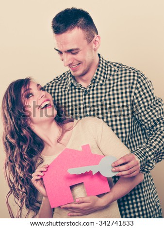 Smiling young couple holding paper house and key. Husband and wife dreaming about new home. Housing and real estate concept. Instagram filtered.