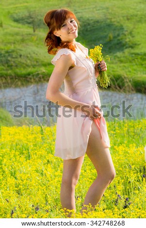 The red-haired girl on meadow with yellow flowers and a smile. The distance we can see the river.