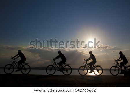 Empty Copy Space Sporty company friends on bicycles outdoors against sunset Silhouette four 4 cyclist going along shoreline coast Reflection sun on water Sport in Nature background Group of people