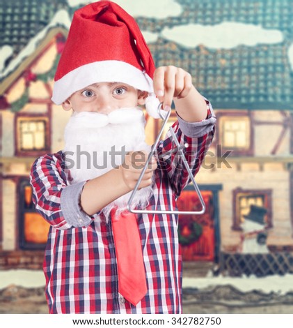 Cute boy dressed up as Santa playing Christmas carols with a triangle. Image with shallow depth of field
