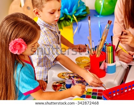Children with teacher woman painting on paper at table  in  kindergarten . Two kids and one adult.