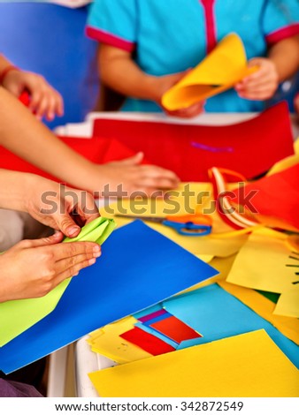 Group hands kids holding colored paper on table in kindergarten .