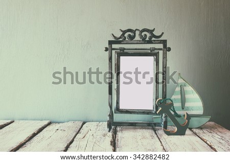 low key image of old victorian steel blue blank frame and wooden sailing boat on wooden table. faded retro filtered image