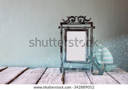low key image of old victorian steel blue blank frame and wooden sailing boat on wooden table. glitter overlay