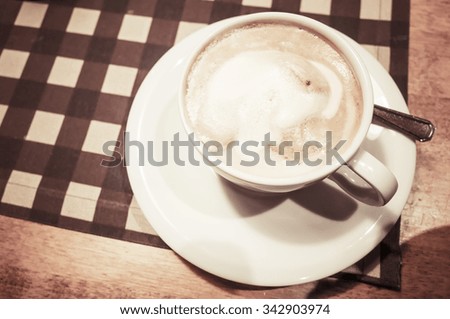 White cup of cappuccino stands on wooden table, retro style warm tonal correction photo filter and selective focus