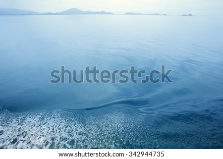 Turbulent spindrift and spray of speeding boat on ocean water surface with wave pattern, coast as blurred background, copy space.
