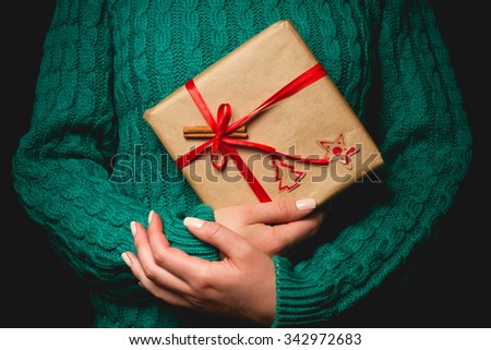 A woman in a green sweater holding a Christmas gift with a red ribbon