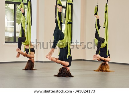 Young women making upside down antigravity yoga exercises. green hammocks