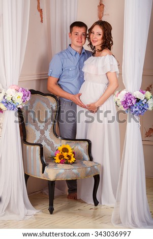 Portrait of expecting couple laughing happily at camera, embracing baby in belly together.