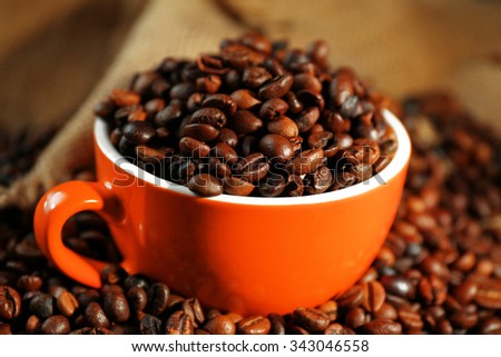A red cup and aromatic coffee beans scattered on sacking background