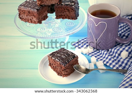 Served table with a cup of tea and chocolate cakes on blue background close-up