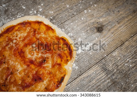 Homemade classic stone baked Margherita Pizza, on a wooden textured background with a dusting of flour