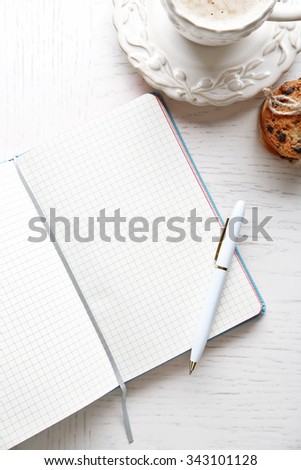 Opened notebook with pile of cookies and cup of coffee on white wooden table